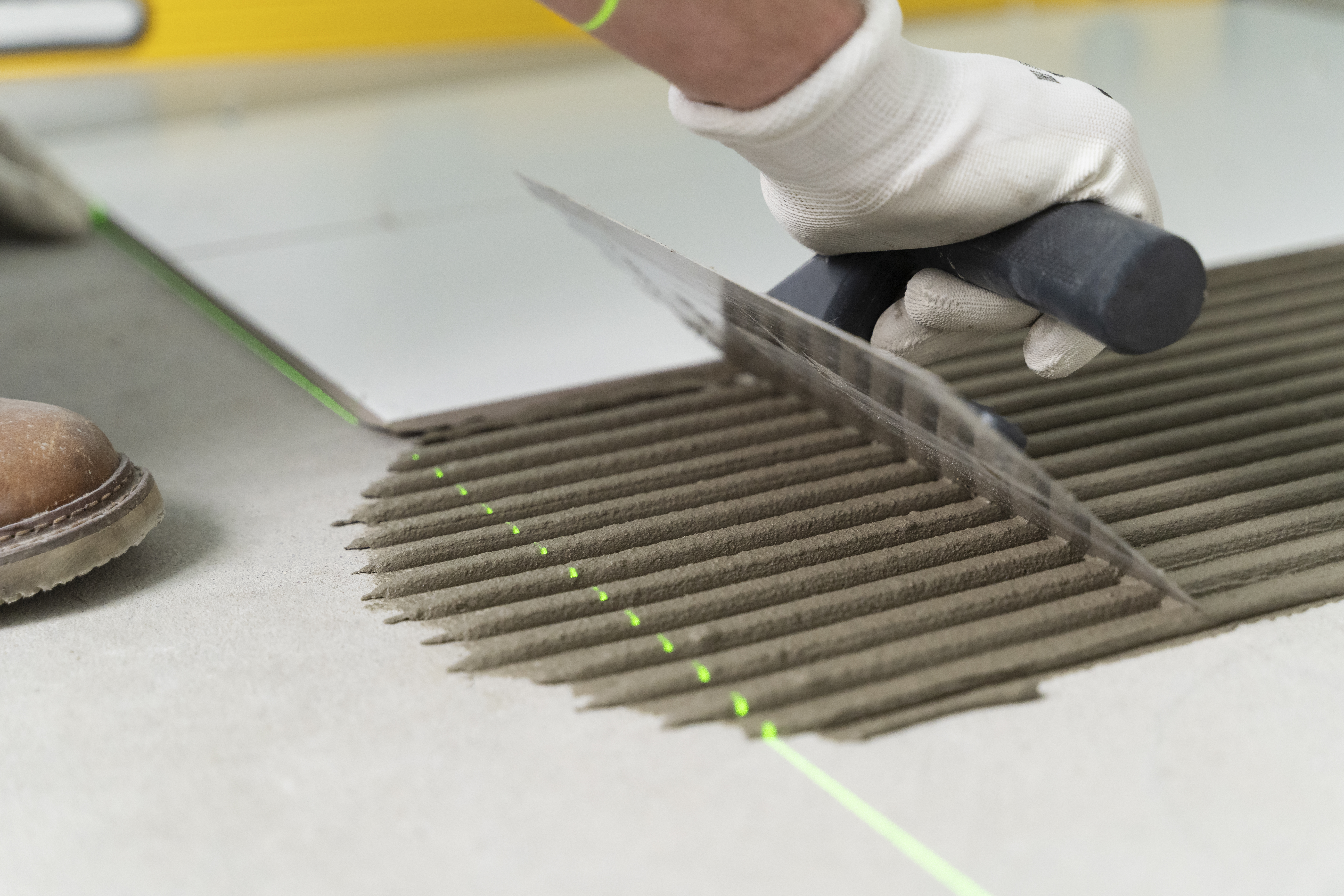 Worker spreading tile adhesive with a notched trowel.