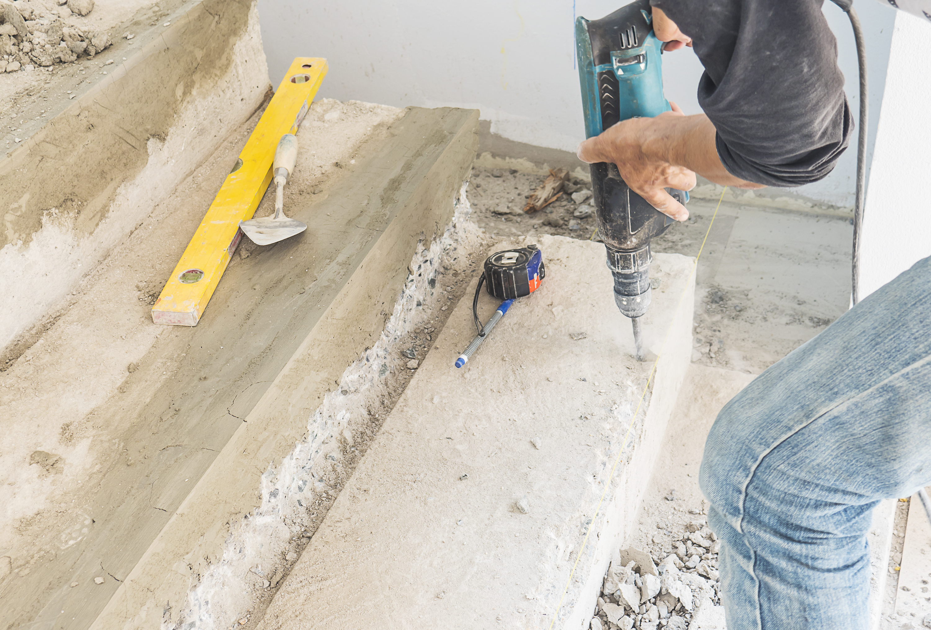 Worker using a drill to repair concrete stairs.